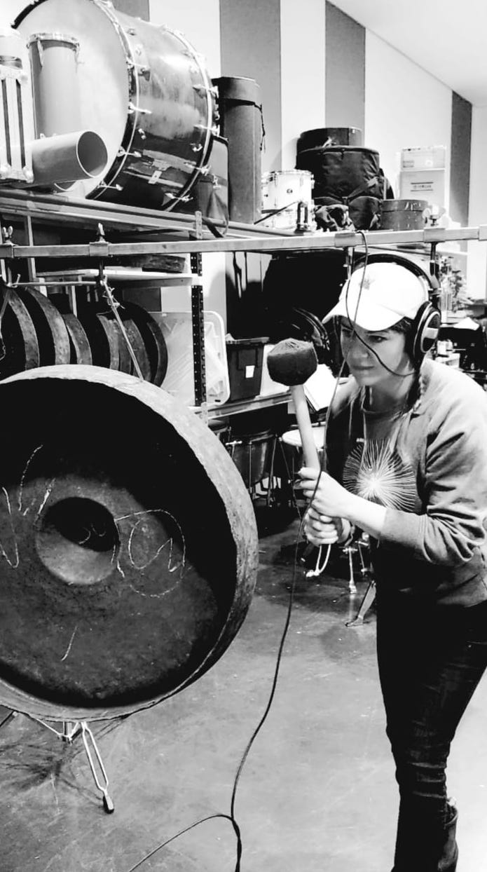 black and white photo of a woman hitting a gong cymbal while recording with perc in the background