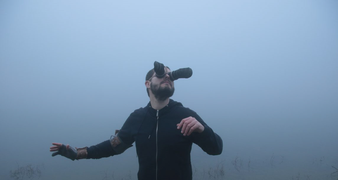 A man surrounded by white fog, wearing a device on his head that moves his visual point of view from the front of the face to the sides of the head.