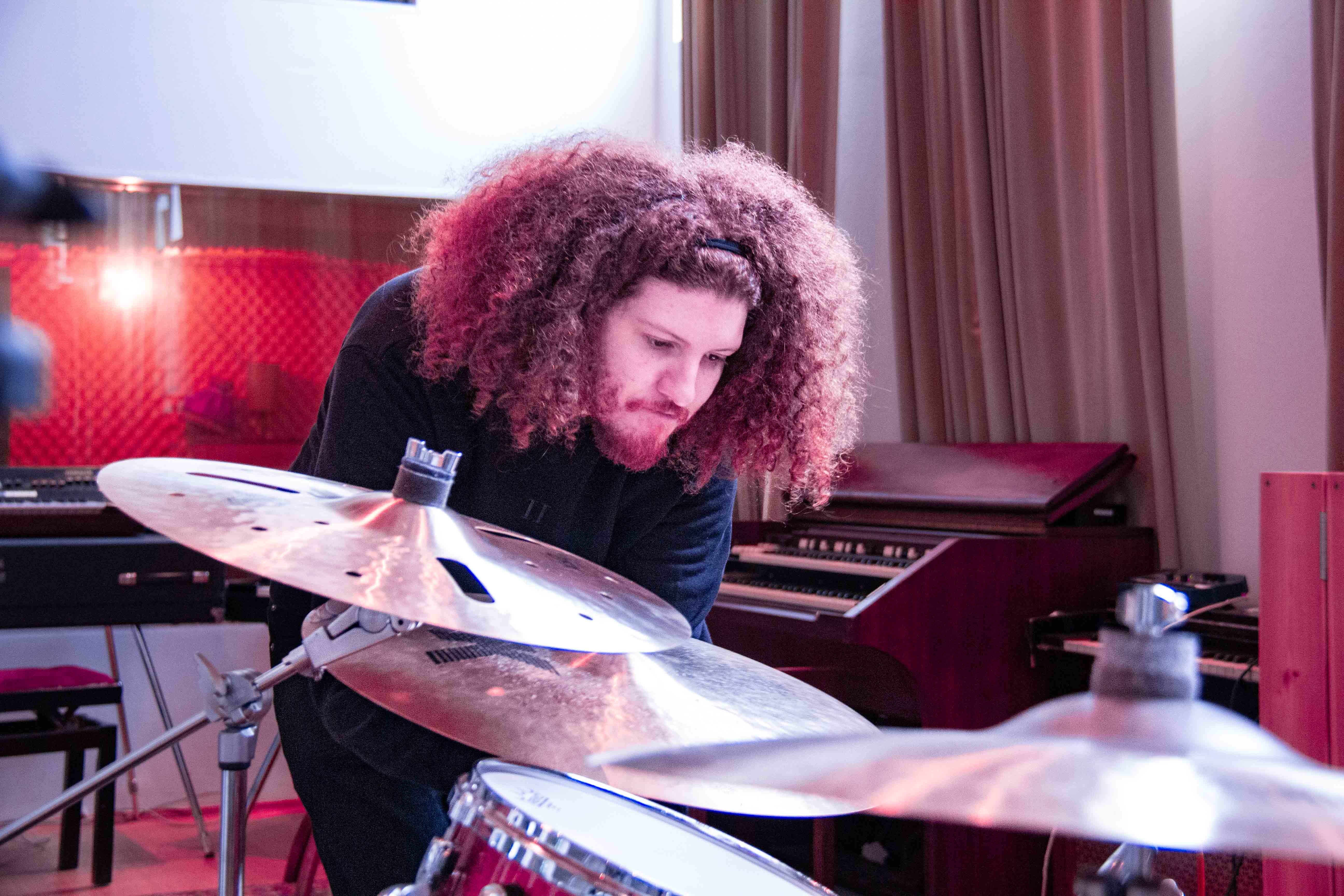 A young man with afro setting up a drum kit in a musical pink lit studio