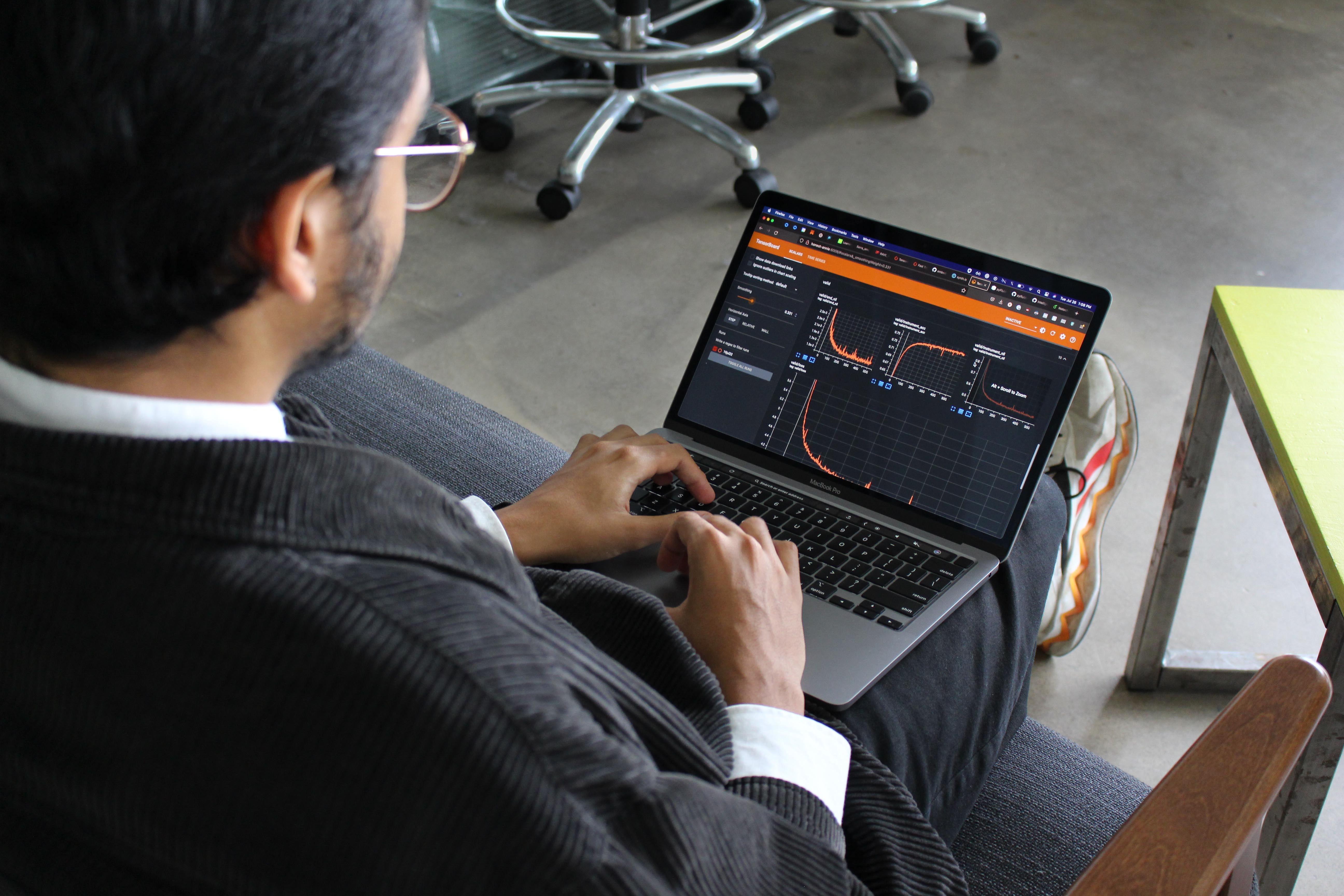 Krish sitting with his laptop showing a dark and orange interface.