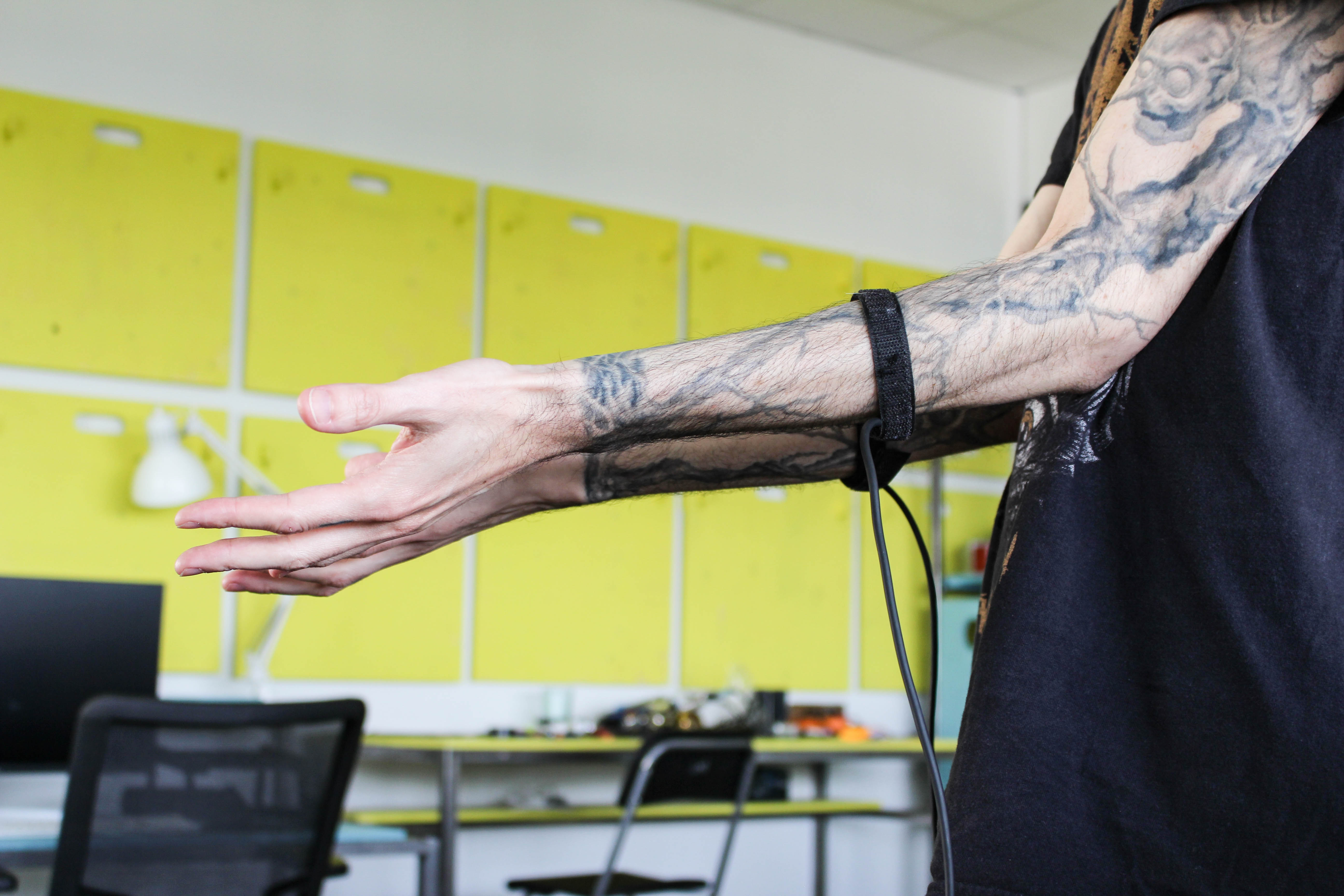 A person holding tattoo covered left arm in front of the camera, sensors are attached