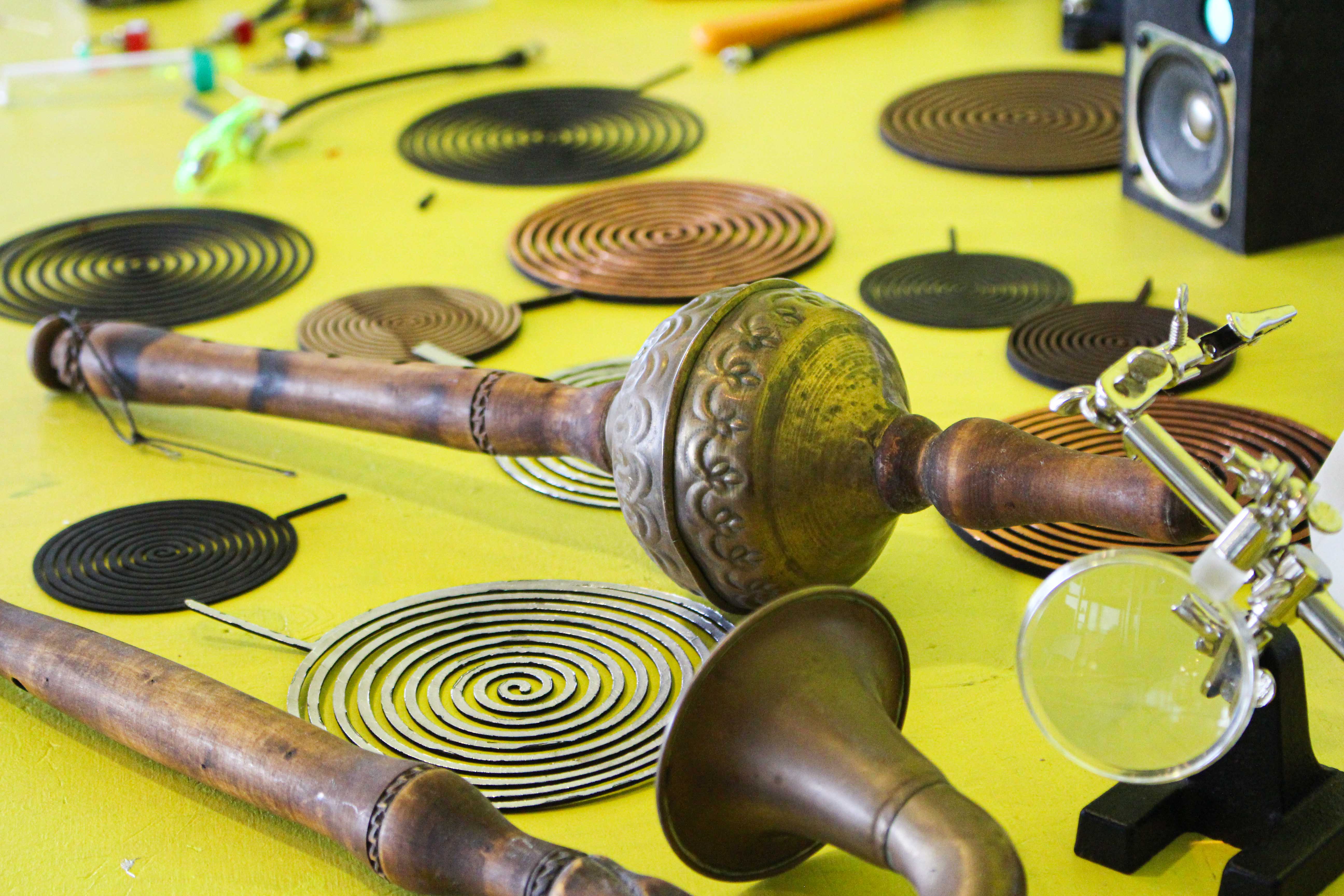 Many different types of instruments and instrumental parts, both acoustic and electronic, placed on a yellow surface.