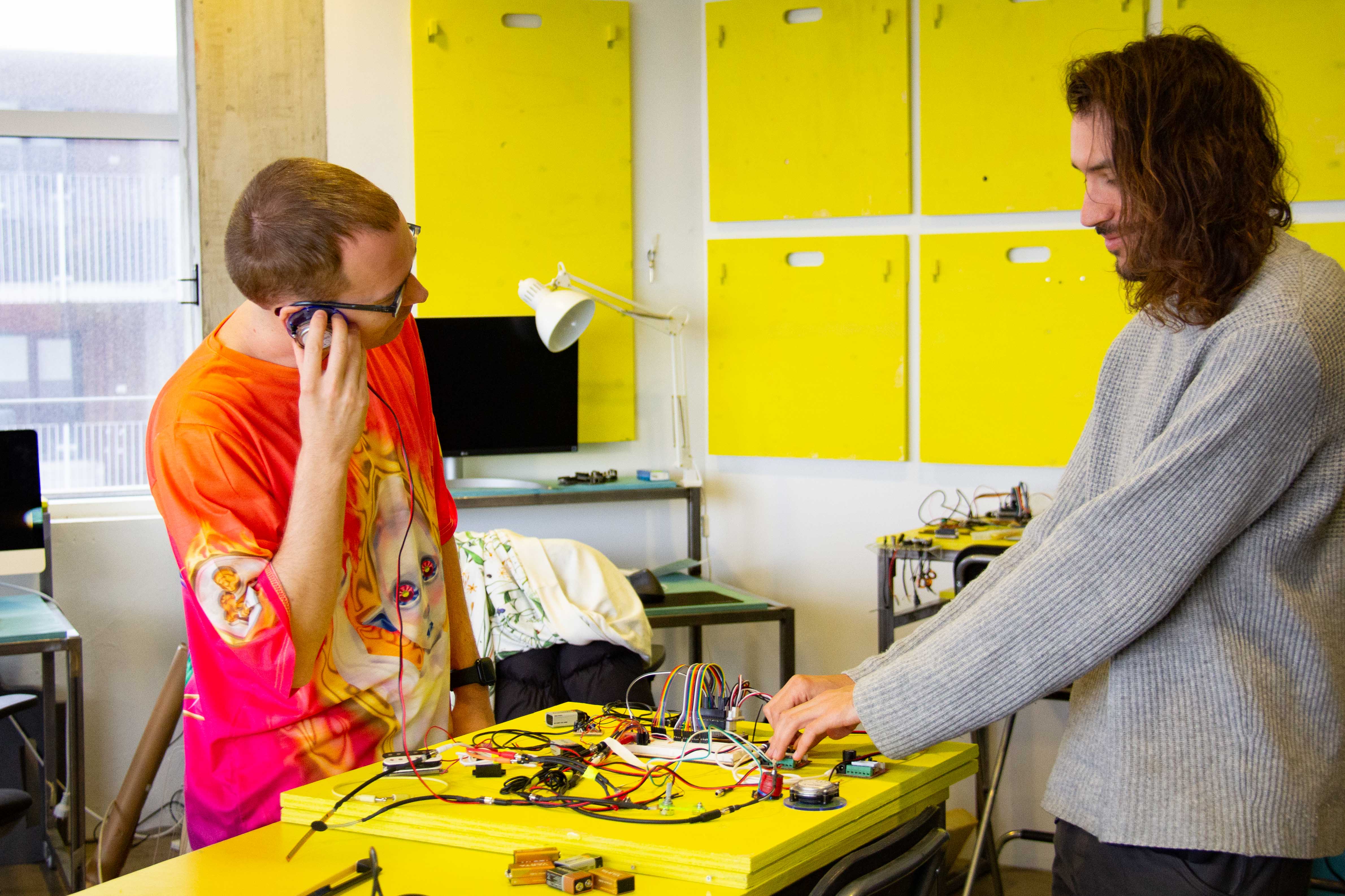 Two young men playing with techincal elements on a yellow table