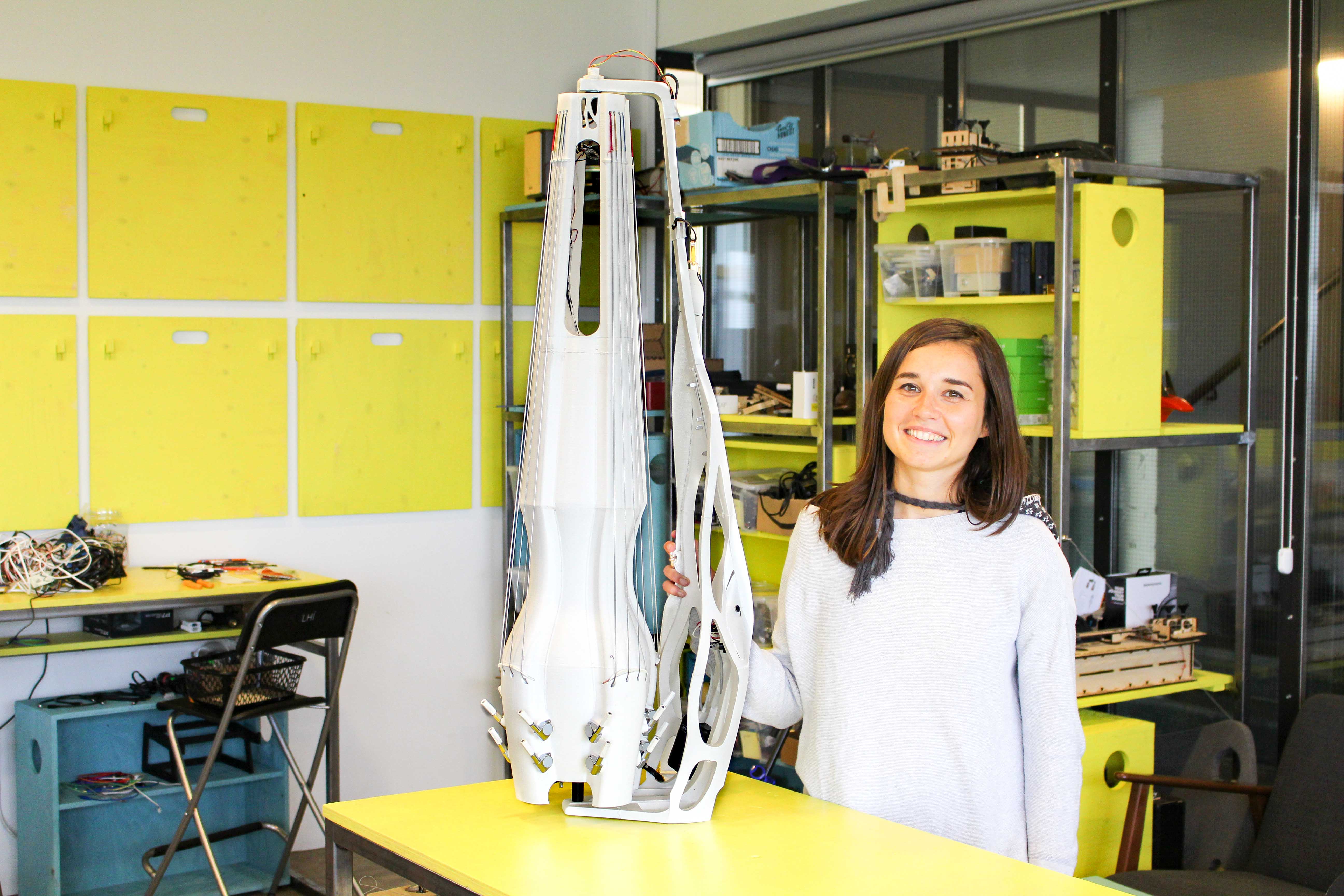 A large white upright instrument on a yellow table, a young woman standing next to it, smiling.