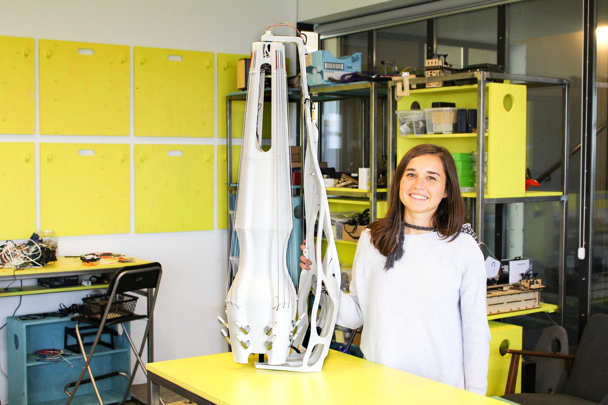 A young woman holding a large white upright instrument in a yellow research lab.