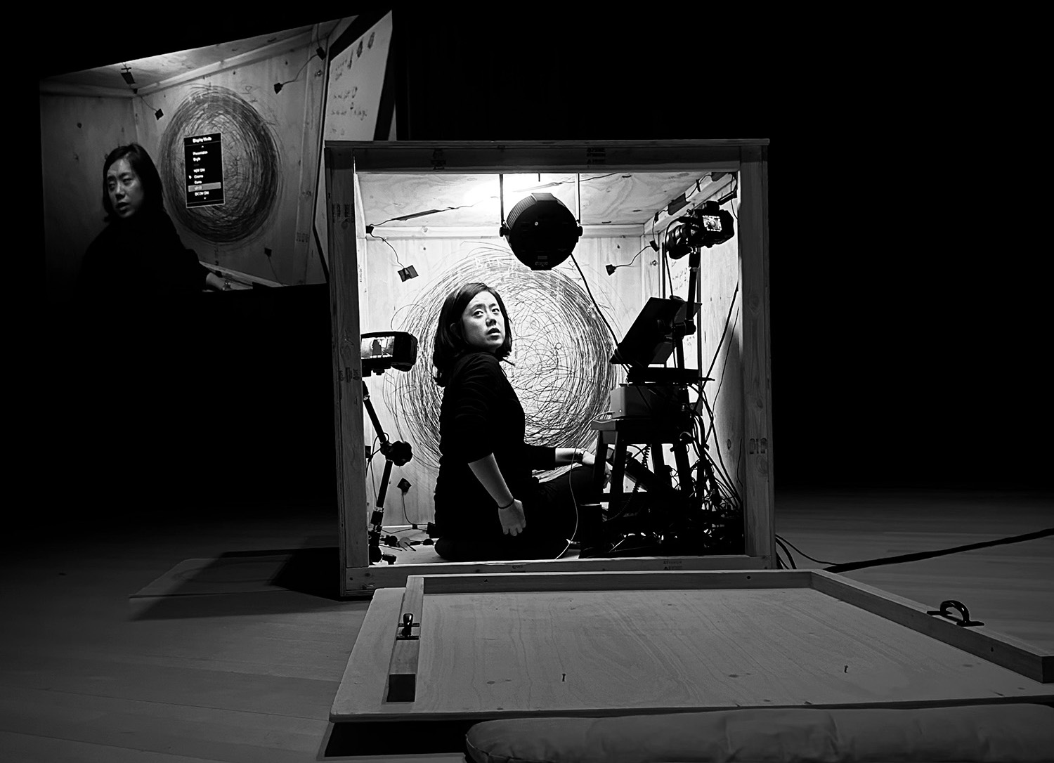 Black and white photo of composer Julie Zhu performing inside of a wooden box.
