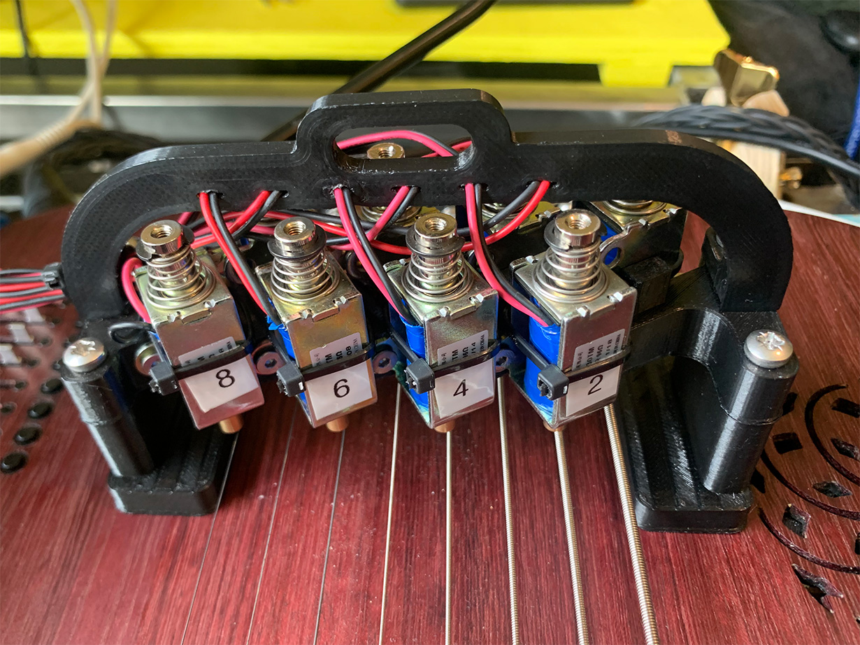 A 3D-printed mount holding a set of solenoids over the strings of the Sophtar instrument.